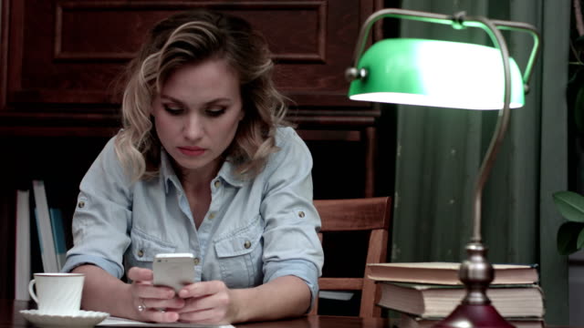 Serious-young-woman-sitting-at-her-workplace-and-typing-an-message-on-her-phone