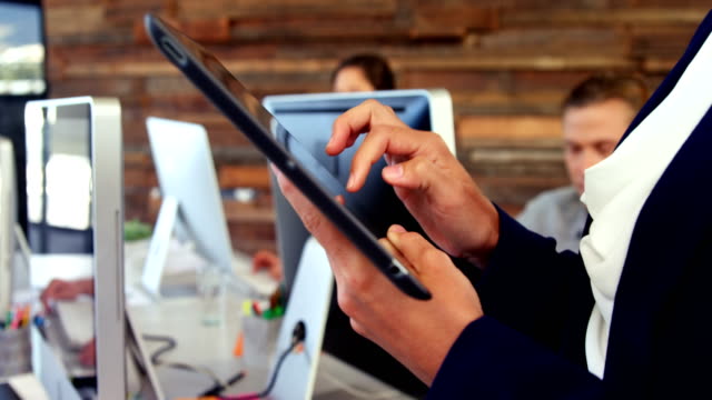 Weibliche-Führungskraft-mit-digital-Tablette-während-Kollege-am-Schreibtisch-arbeiten