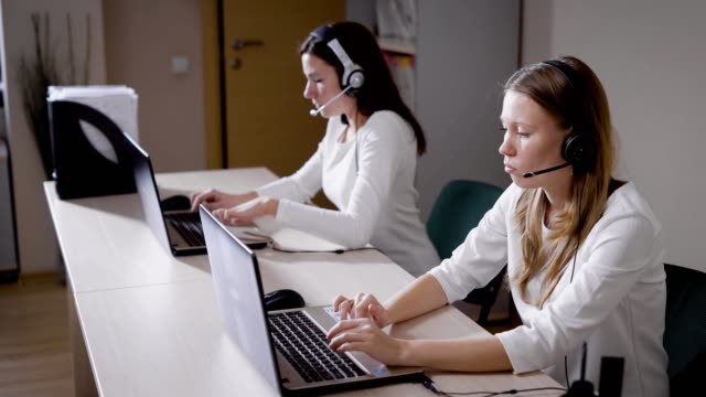 Varias-mujeres-impresión-el-texto-en-el-teclado-del-ordenador-portátil,-la-charla-de-las-señoras-en-el-micrófono-en-la-oficina-de-centro-de-llamada,-contestar-las-llamadas-entrantes-y-asesorar-a-los-clientes