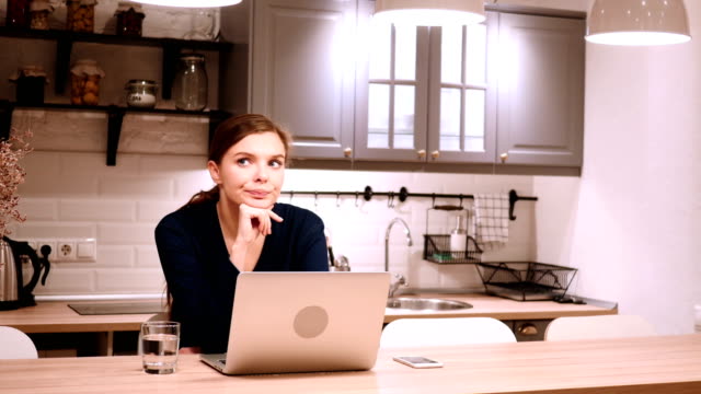 Mujer-pensativa-pensando-y-trabajando-en-línea-en-cocina