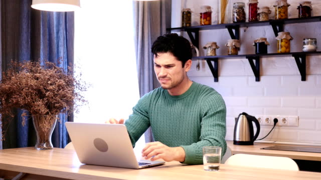 Depressed-Man-Upset-by-Loss-Working-on-Laptop,-Sitting-in-Kitchen