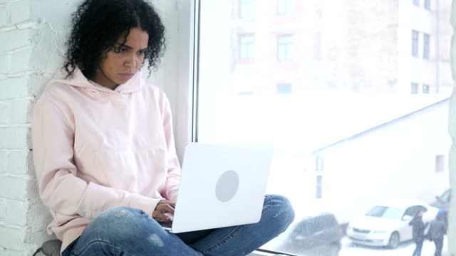Afro-amerikanische-Frau-denken-und-arbeiten,-sitzen-am-Fenster