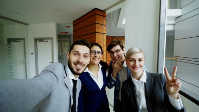 POV-of-Happy-business-team-taking-selfie-portrait-on-smartphone-camera-and-posing-for-group-photo-during-meeting-in-modern-office