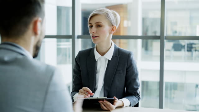 HR-Geschäftsfrau-Vorstellungsgespräch-mit-jungen-Mann-im-Anzug-und-dabei-seinen-Lebenslauf-Anwendung-in-modernen-Büro