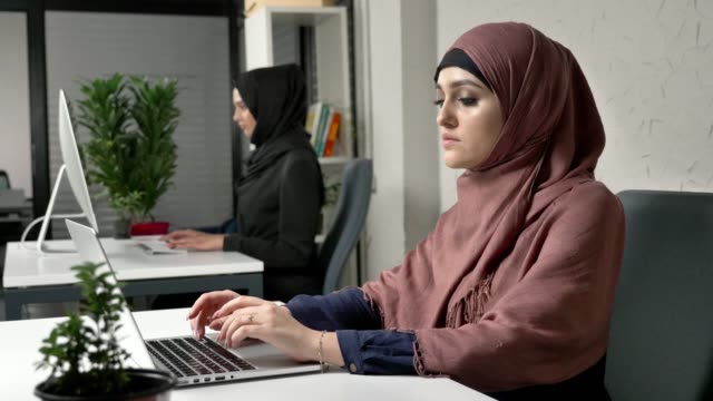 Zwei-schöne-junge-Mädchen-in-Hijabs-arbeiten-im-Büro,-auf-Computern.-Arabische-Frauen-im-Büro.-Fucus-ziehen-60-fps