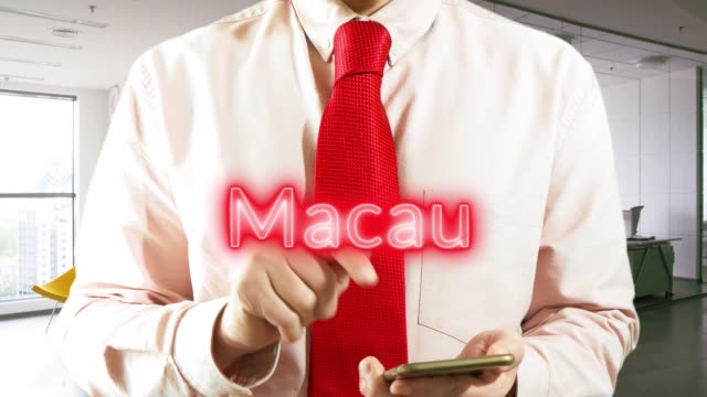 Macau.-Businessman-chooses-а-city-on-virtual-interface-in-light-office.-Concept:-business-trip,hologram,-technology,-augmented-reality,-future,-travel