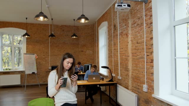 Hermosa-mujer-bebiendo-café-smartphone-en-la-oficina-moderna-loft