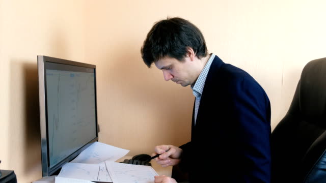 Hombre-trabaja-en-una-computadora.-Compara-gráficos-en-la-pantalla-y-en-papel.
