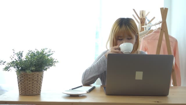 Schöne-junge-lächelnde-Frau-arbeiten-am-Laptop-und-genießen-Sie-warme-Kaffeetrinken-in-einem-Wohnzimmer-zu-Hause-sitzen.-Zeit-zu-Hause-genießen.-Asiatische-geschäftsfrau-in-ihrem-home-Office-arbeiten.