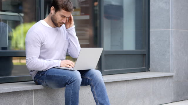 Angespannte-gut-aussehender-Mann-mit-Kopfschmerzen-arbeiten-am-Laptop-sitzt-draußen-Büro
