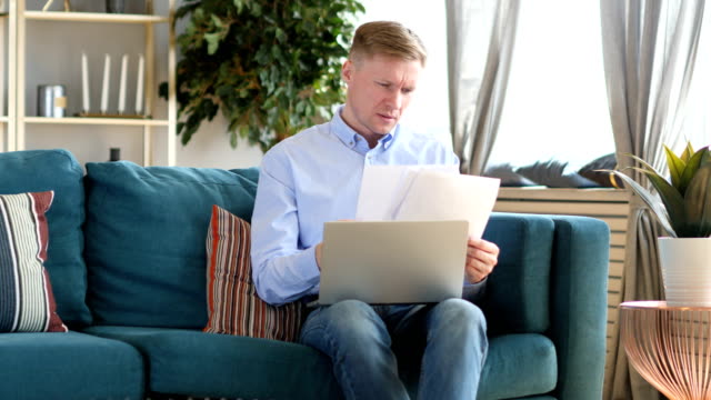 Middle-Aged-Man-Working-on-Documents-and-Laptop