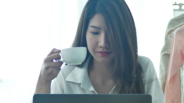 Schöne-junge-lächelnde-Frau-arbeiten-am-Laptop-und-genießen-Sie-warme-Kaffeetrinken-in-einem-Wohnzimmer-zu-Hause-sitzen.-Zeit-zu-Hause-genießen.-Asiatische-geschäftsfrau-in-ihrem-home-Office-arbeiten.