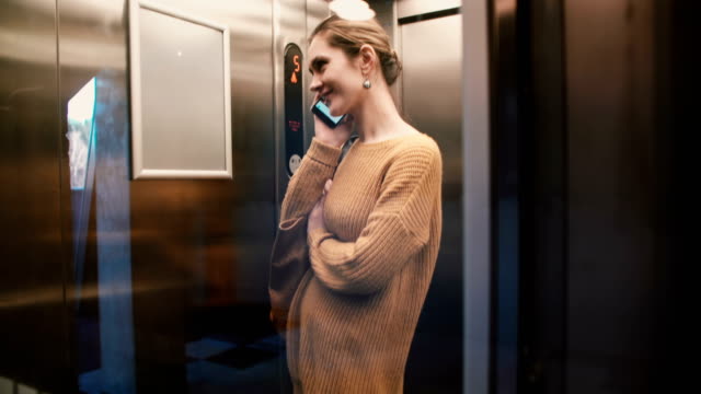 Ein-Blick-auf-jungen-entspannt-Europäerin-Reiten-bis-in-transparentem-Glas-Wand-Aufzug-am-Telefon-sprechen-und-Lächeln
