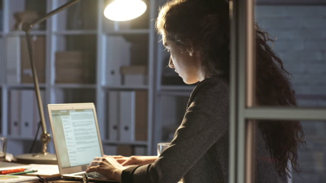 Junge-weibliche-Büroangestellte-schreiben-auf-Computer-in-der-Nacht