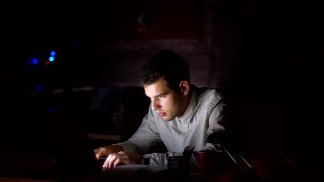 Netter-kaukasischer-Mann-ist-müde-vom-Tippen-auf-Laptop,-angefangen-beim-Einschlafen-neben-dem-Bildschirm-beim-Sitzen-am-Arbeitsplatz-im-dunklen-Büro,-schwarzer-Hintergrund
