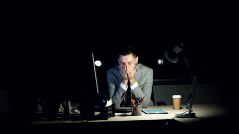 Weary-guy-office-worker-is-working-on-computer-late-at-night-meeting-deadline-looking-tired-and-exhausted.-Hard-working-youth,-technology-and-stress-concept.