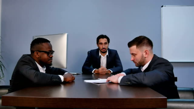 Young-serious-man-holding-papers,-reading-them-attentively,-during-meeting-in-office