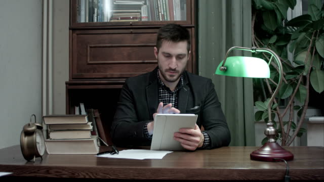 Junger-Mann-mit-Bücher-mit-digital-Tablette-im-Hause-Zimmer-Büro-am-Schreibtisch-sitzen
