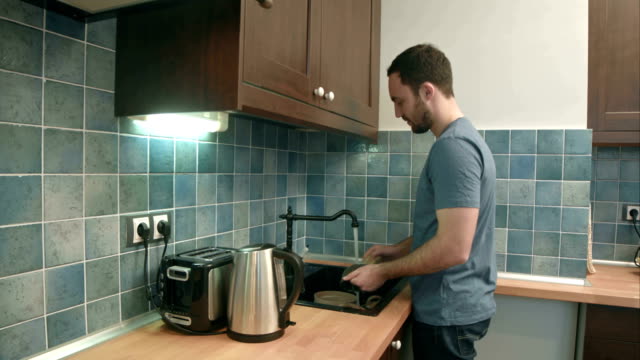Young-man-washing-dishes-in-the-kitchen-at-home