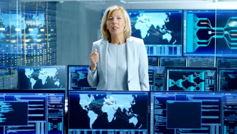 Im-System-Control-Room-weiblich-Chief-Engineer-beschreibt-ihr-Projekt-in-die-Kamera-sprechen.-Im-Hintergrund-mehrere-Bildschirme,-interaktive-Daten.