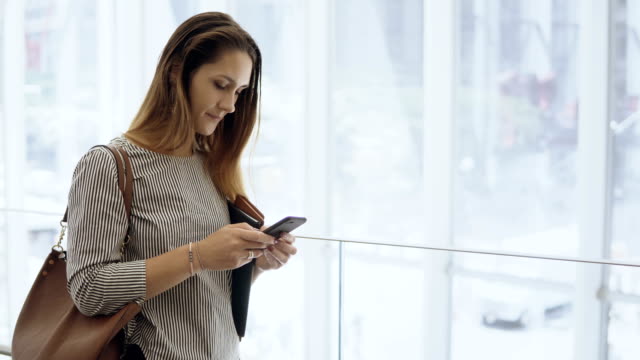 Young-beautiful-businesswoman-using-the-smartphone-in-office-building.-Busy-female-going-down-on-escalator