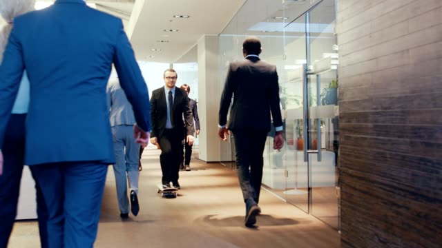 Stylish-Suited-Businessman-Rides-Skateboard-Through-the-Corporate-Building-Hallway.-Stylish-Glass-and-Concrete-Building-with-Multicultural-Crowd-of-Business-People.