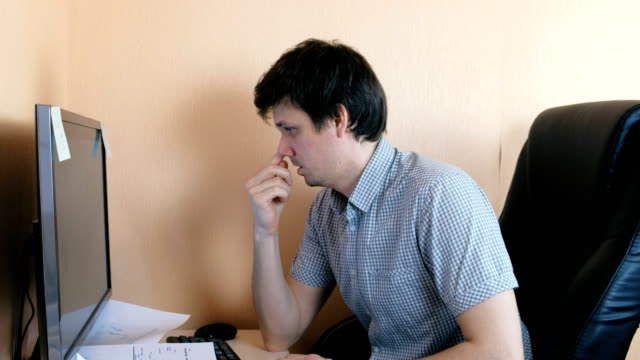 Hombre-joven-escoge-su-nariz-trabajando-en-la-computadora.