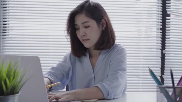 Hermosa-joven-sonriente-mujer-asiática-trabajando-en-ordenador-portátil-mientras-está-sentado-en-una-sala-de-estar-en-casa.-Mujer-de-negocios-asiáticos-trabajando-en-su-oficina-en-casa.-Disfrutando-en-casa.