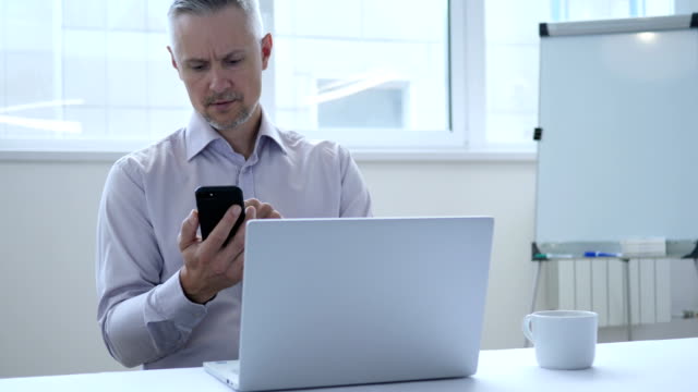 Middle-Aged-Businessman-Busy-Using-Smartphone-for-Work-in-Office