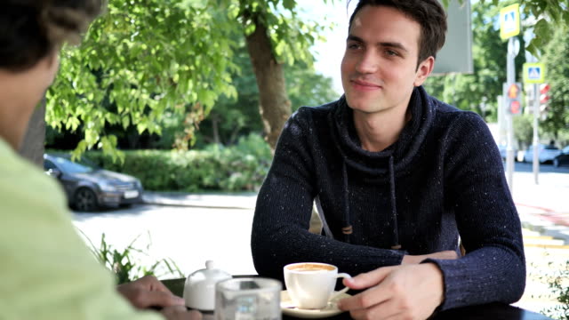 Junge-Mann-im-Gespräch-mit-Freund-beim-Sitzen-im-Cafe-Terrasse