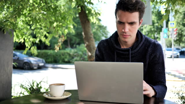 Junge-Mann-Tippen-auf-Laptop-beim-Sitzen-im-Cafe-Terrasse
