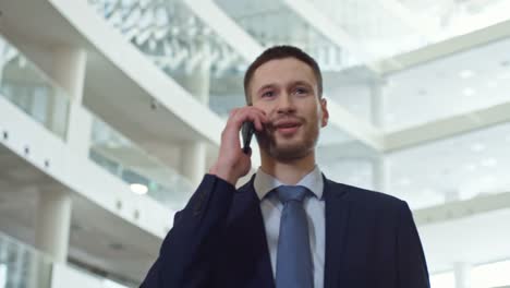 Young-Man-Walking-and-Speaking-on-Phone-in-Business-Center
