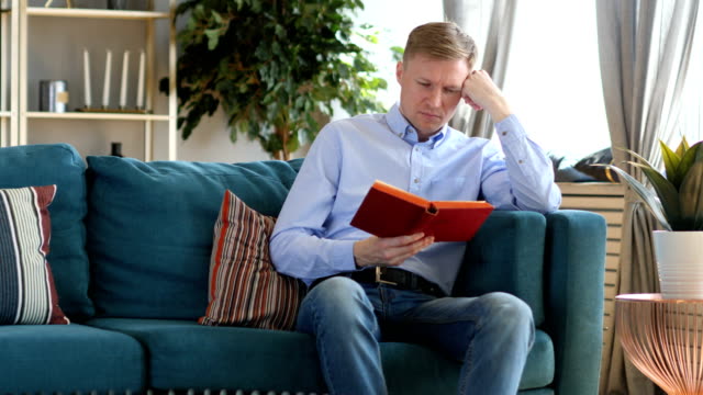 Middle-Aged-Man-Sleeping-while-Reading-Book,-Sitting-on-Sofa