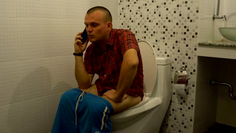 A-man-sits-on-a-toilet-and-talking-on-the-phone