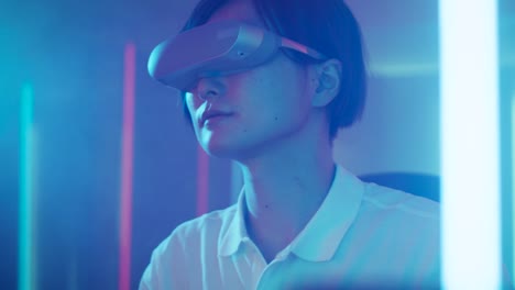 Ostasiatische-Pro-Gamer-Virtual-Reality-Kopfhörer-tragen-spielt-online-Videospiel-mit-Joysticks-/-Controller.-Coole-Retro-Neon-Farben-in-den-Raum.