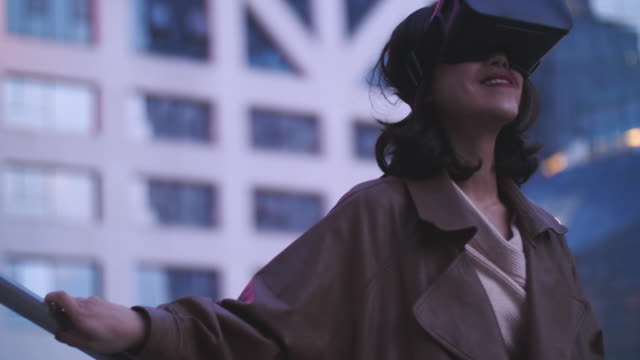 Slow-Motion-für-eine-hübsche-junge-Asiatin-mit-VR,-virtual-Reality-Kopfhörer-im-Freien-im-Stadtpark