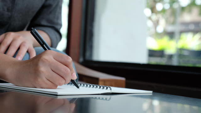 Die-Hand-einer-Frau-auf-einem-weißen-leeren-Notebook-auf-Tabelle-aufschreiben