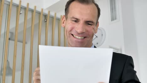 Middle-Aged-Businessman-Celebrating-Success-while-Reading-Documents-in-Office