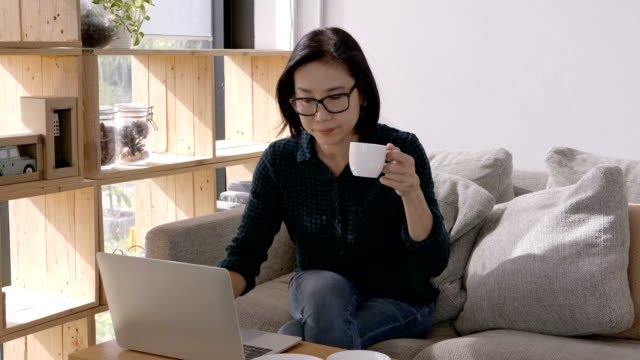 Schöne-Asiaten-junge-Frau,-arbeiten-mit-Computer-Laptop-und-Kaffeetrinken-beim-Sitzen-auf-dem-Sofa-zu-Hause.-Arbeit-zu-Hause-Konzept