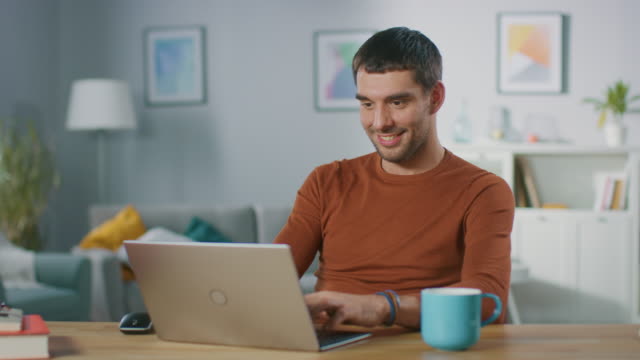 Retrato-de-sonriente-guapo-trabajando-en-ordenador-portátil,-sentado-en-su-escritorio-de-madera-en-casa.-Hombre-navegando-por-Internet,-trabajando-en-la-Notebook-de-su-oficina-de-sala-de-estar.