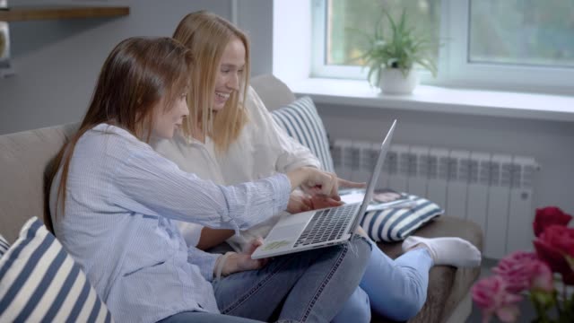paar-Freunde-Mädchen-sitzen-auf-einer-Couch-in-Haus-und-Online-shopping,-diskutieren-und-runden-Laptop-festhalten
