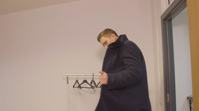 Young-business-man-entering-in-office-taking-off-coat-and-hanging-on-hanger