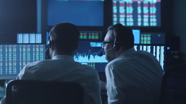 Team-of-stockbrokers-are-having-a-discussion-in-a-dark-office-with-display-screens.
