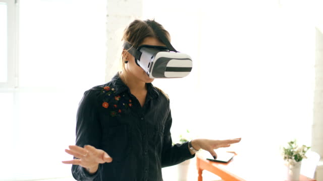 Frau-in-VR-Kopfhörer-nachschlagen-und-versucht,-tippen-Sie-auf-Objekte-in-der-virtuellen-Realität-zu-Hause-drinnen