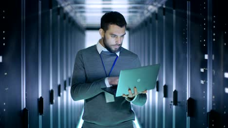 Male-IT-Engineer-Works-on-a-Laptop-in-a-Big-Data-Center.-Rows-of-Rack-Servers-are-Seen.