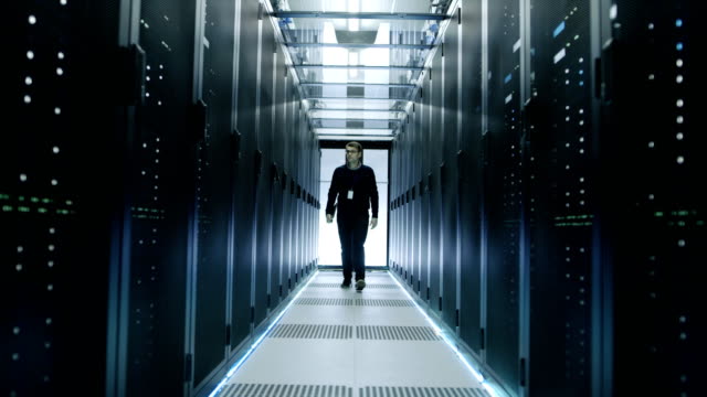 Frontal-View-of-IT-Engineer-Walking-Through-Data-Center-with-Working-Rack-Servers.