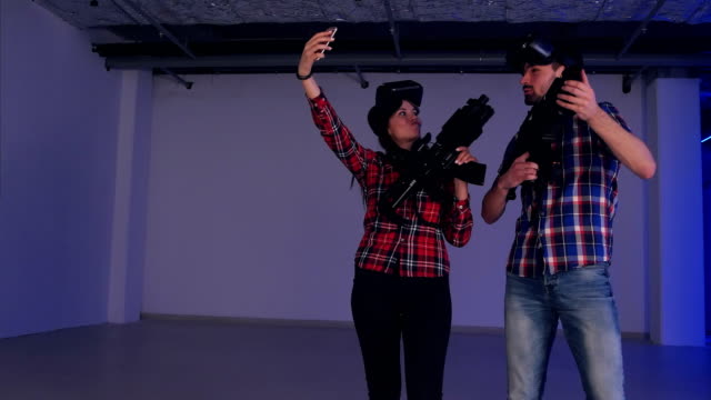 Joven-pareja-vistiendo-gafas-de-realidad-virtual-y-pistolas-tomando-selfies-en-el-teléfono
