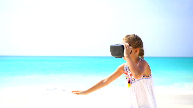 Cute-little-child-girl-using-VR-virtual-reality-goggles.-Adorable-girl-look-into-the-virtual-glasses-on-white-beach
