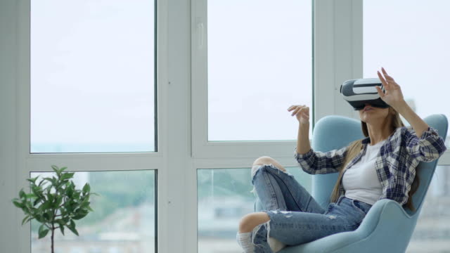Young-woman-have-VR-experience-using-virtual-reality-headset-sitting-in-chair-on-balcony