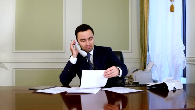 Young-confident-successful-businessman-working-in-modern-office-analyzing-business-by-phone-conversation